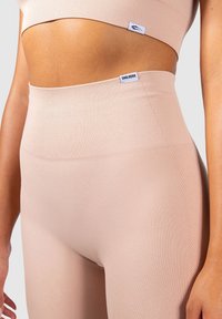 Set di abbigliamento attivo seamless a coste in beige chiaro, composto da un top cropped e leggings a vita alta, con etichette di branding visibili. Texture liscia.