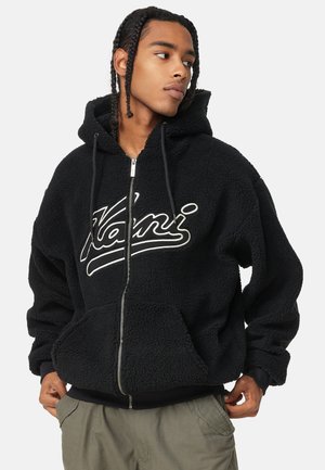 Black fleece hoodie with a front zip, large kangaroo pockets, and a white scripted logo. Features a lined hood and ribbed cuffs.