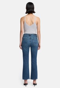 Canottiera grigia a coste con spalline sottili abbinata a jeans in denim blu svasati con orlo grezzo e tasche posteriori con cuciture decorative.