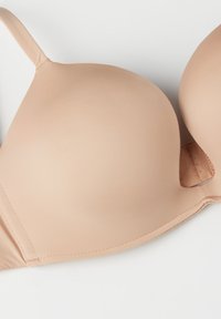 Beige gepolsterde beha met een naadloos ontwerp, verstelbare bandjes en een zachte textuur. Voorzien van een zijsluiting voor een sluiting zonder zichtbare lijnen.