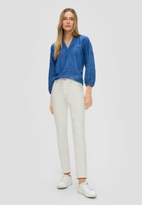 Niebieska bluzka z długim rękawem i dekoltem w kształcie litery V, zestawiona z jasnymi, dopasowanymi dżinsami i białymi trampkami. Tkaniny wydają się miękkie o gładkiej fakturze.