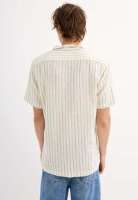 Camisa de manga corta, ligera, con rayas verticales en crema, rojo y azul. Presenta un cuello clásico y un dobladillo recto.