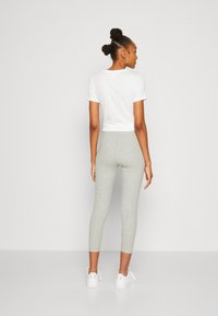Camiseta blanca recortada y leggins gris claro. Los leggins son ajustados y tienen una textura suave. Zapatillas blancas completan el conjunto.