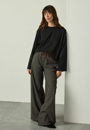 Cămașă neagră cu mâneci lungi, asortată cu pantaloni largi gri cu un model, care au un elastic la talie și detalii cu șnur.