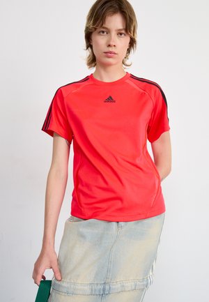 T-shirt de sport rouge à manches courtes, accents noirs et logo sur la poitrine. Tissu lisse avec une coupe ajustée.