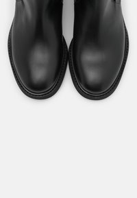 Bottines noires en cuir avec une finition lisse, forme de bout arrondi et détails de couture minimaux le long de la semelle et des bords supérieurs.
