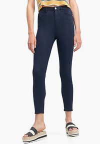 Jeans skinnies azul marino con un diseño de cintura alta, tela elástica y costuras minimalistas. Combinados con sandalias a rayas en blanco y negro.