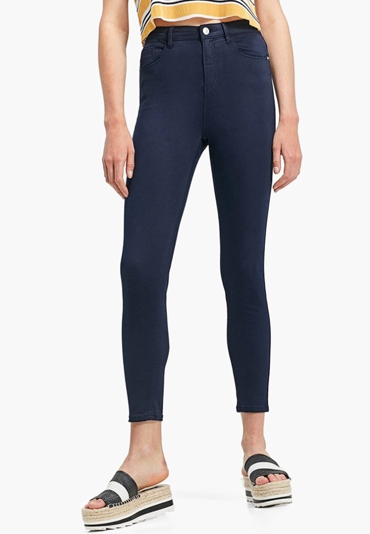 Jeans skinnies azul marino con un diseño de cintura alta, tela elástica y costuras minimalistas. Combinados con sandalias a rayas en blanco y negro.