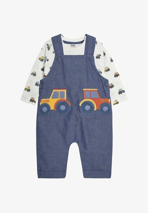 Traper overall s dva šarena aplikacija traktora sprijeda, uparen s dugom bijelom majicom s printom traktora po cijeloj površini.