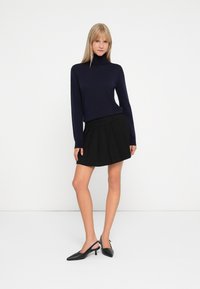 Navy turtleneck sweater, black pleated skirt, and black slingback heels. Smooth knit material, fitted design, and mid-thigh skirt length.