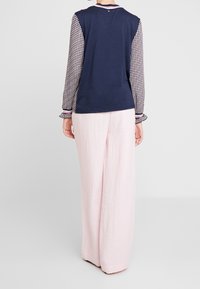 Langarmshirt met een marineblauw lichaam en patroon op de mouwen. Gecombineerd met losse roze broek. Heeft een ronde halslijn en subtiele details aan de achterkant.
