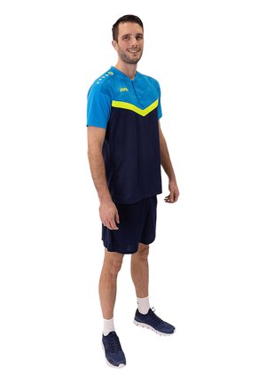 De sportoutfit voor heren heeft een blauw en marinekleurig kleurenpalet met een gele chevronontwerp. Gemaakt van lichte stof, inclusief shorts en sportschoenen.