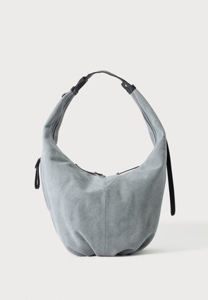Weiche graue Wildleder-Hobo-Tasche mit schwarzen Lederakzenten und Reißverschluss, vor einem einfarbigen hellen Hintergrund dargestellt.
