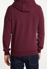 Sudadera burdeos con capucha ajustable, puños y dobladillo acanalados. Textura suave, diseño ajustado y vista trasera que muestra la tela suave.