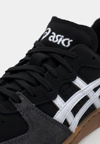 Black suede sneaker with white stripes, featuring a textured upper, round laces, and a rubber sole. ASICS logo on the tongue.
