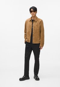 Rjava zamšasta jakna s ostrim ovratnikom, sprednjimi gumbi in žepom na prsih. Obuta je čez črno srajco in je kombinirana s črnimi hlačami ter čevlji.