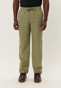 Pantaloni din in de culoare verde măsliniu, ușori, cu un elastic la talie, detalii cu șnur și o croială lejeră. Prezintă picioare drepte și o textură subtilă.