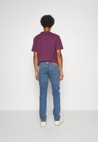 Lila t-shirt med kort ärm i kombination med blå denimjeans. Jeansen har en läderlapp på den bakre högra fickan och en klassisk passform.