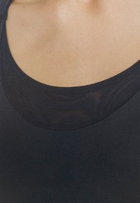 Top atlético preto com um decote de malha texturizada. O tecido parece suave, ajustado e elástico, adequado para roupas de desporto.