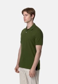 Polo verde con colletto, maniche corte e un piccolo logo sul petto. Realizzato in un tessuto liscio ed elasticizzato con fessure laterali.