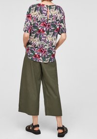 Blusa con motivo floreale in tessuto leggero con apertura a goccia sulla schiena, abbinata a pantaloni a gamba larga verde oliva e sandali neri con cinturini.
