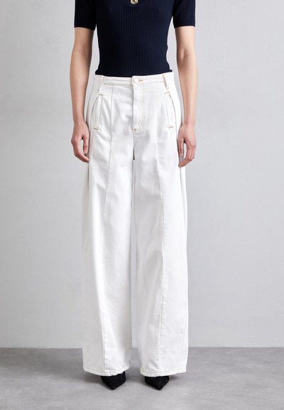 Pantalons blancs à large jambe avec poches avant et coutures contrastées, associés à un haut ajusté en ribbed bleu marine. Tissu texturé, design minimaliste.