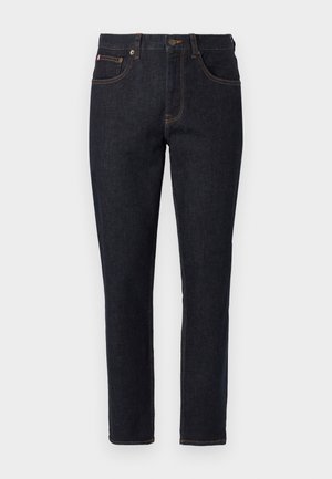 Σκούρο μπλε τζιν σε εφαρμοστή γραμμή με εμπρόσθιες τσέπες, βρόχους ζώνης και πορτοκαλί ραφές σε απλό φόντο.