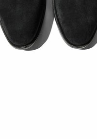 Zapatos de ante negro con punta afilada y textura suave. Las suelas presentan un borde delgado y contrastante para añadir detalle y estructura.