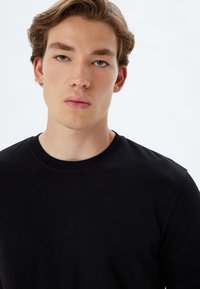 Sort bomulds T-shirt med rund hals, korte ærmer og en glat overflade. Stoffet er let og tætsiddende, med minimale sømme.