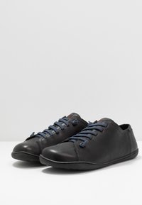 Zapatos de cuero negros con puntas redondeadas, cordones azules y un diseño minimalista; textura suave y suela flexible para mayor comodidad.