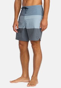 Pánské plavky v modrém gradientu s vodorovnými pruhy. Lehká látka, elastický pás se šňůrkou, postranní kapsy, nášivka s logem.