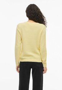 Κίτρινο πουλόβερ με υφή, στρογγυλή λαιμόκοψη και μακριά μανίκια, με ριμπ μανσέτες και τελείωμα, συνδυασμένο με μαύρο παντελόνι.