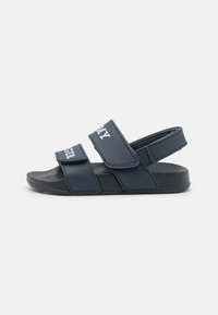Sandali blu scuro con due cinturini regolabili in Velcro, dotati di una soletta texture e una suola piatta in gomma. Nessun motivo o accento visibile.