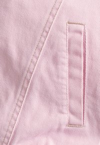 Růžová bavlněná látka se šikmým žebrováním a náprsní kapsou, s kontrastním prošíváním podél švu a okrajů kapsy.