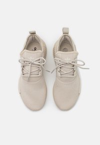 Beige athletic shoes with a breathable mesh upper, flat laces, and a textured sole, featuring a logo on the tongue and heel pull tab.