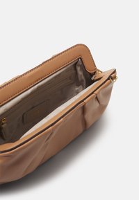 Pochette en cuir synthétique beige avec fermeture éclair, poche intérieure et doublure à motif subtil. Texture douce, bords arrondis et accents de ferrures dorées.