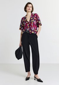 Camicia a maniche corte, colorata con stampa floreale, pantaloni a vita alta neri, décolleté neri a punta con dettagli decorativi e una pochette nera.