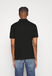 Svart pikétröja med krage, korta ärmar, slät yta och rak nederkant. Buren med blå jeans, vilket visar en avslappnad design.