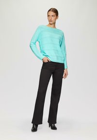 Pull turquoise à côtes avec des manches longues et un large col, associé à un pantalon noir ajusté et des bottines à talons noires.