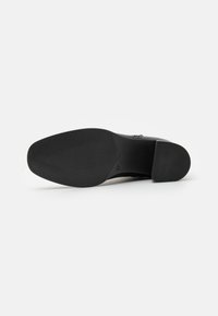Schwarze Ledersohle mit einem strukturierten Griffmuster und leicht erhöhtem Absatz. Verfügt über eine glatte Oberfläche und ein rundes Zehendesign.