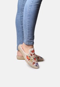 Scarpe slip-on ricamate con un design floreale in rosso, giallo e blu su una tomaia in tessuto beige e una suola in juta testurizzata.