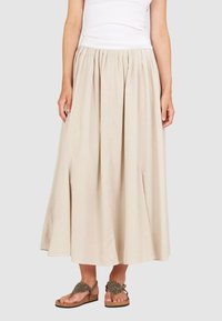 Beige, knöchellange Rock mit gerafftem Taillenbund und zwei seitlichen Schlitzen; leichtes Material; kombiniert mit verzierten Sandalen.