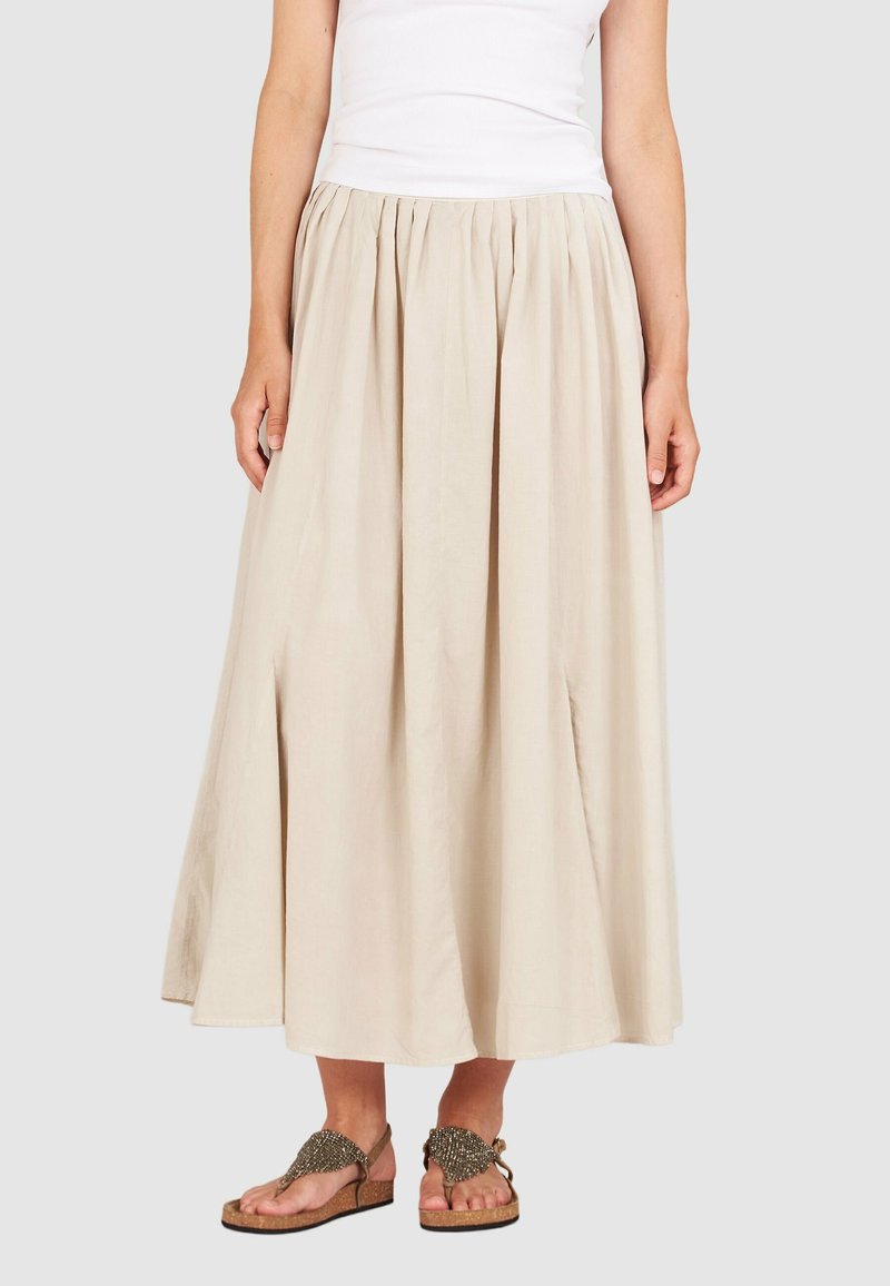 Beige, knöchellange Rock mit gerafftem Taillenbund und zwei seitlichen Schlitzen; leichtes Material; kombiniert mit verzierten Sandalen.