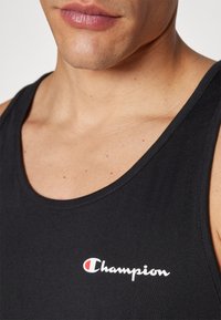Črn bombažni tank top z okroglo izrezom, ki ima logo "Champion" v beli in rdeči barvi na levi strani prsnega koša.