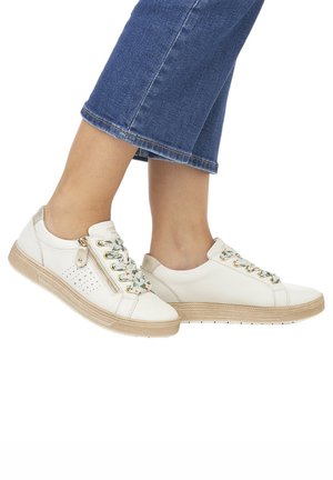 Baskets en cuir blanc avec des lacets décoratifs multicolores, une fermeture éclair sur le côté, un design perforé et une semelle crème. Portées avec un jean cropped bleu.