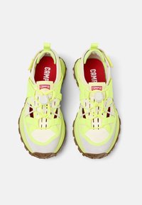 Sneakers Camper gialli e bianchi con solette rosse, suole robuste marroni e lacci elastici bungee con fermagli bianchi, visti dall'alto.