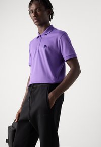 Lila polotröja med korta ärmar och krage, med en svart logotyp. Kombinerad med svarta joggerbyxor, slät textur och sidfickor.