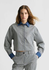 Blaues Karomuster-Crop-Shirt mit kontrastierendem Denim-Kragen und -Manschetten; langärmlig und mit Knopfleiste. Das Muster zeigt ein kleines kariertes Design.