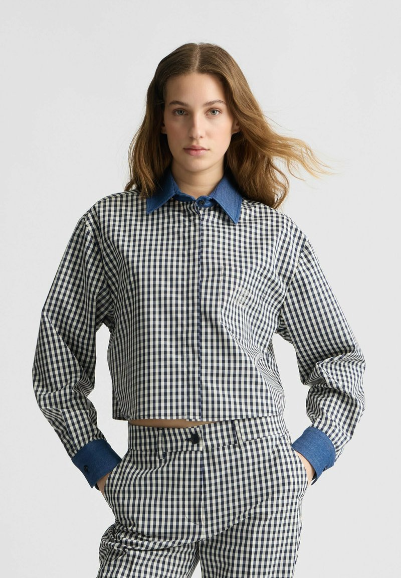 Blaues Karomuster-Crop-Shirt mit kontrastierendem Denim-Kragen und -Manschetten; langärmlig und mit Knopfleiste. Das Muster zeigt ein kleines kariertes Design.