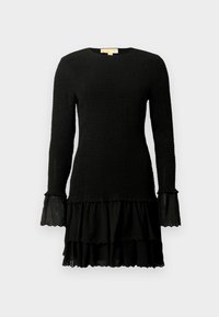 Vestido negro de manga larga, con un cuerpo texturizado y un dobladillo con volantes en capas. Acentos de tela transparente con bordes en forma de ondas en los puños de las mangas y el dobladillo.